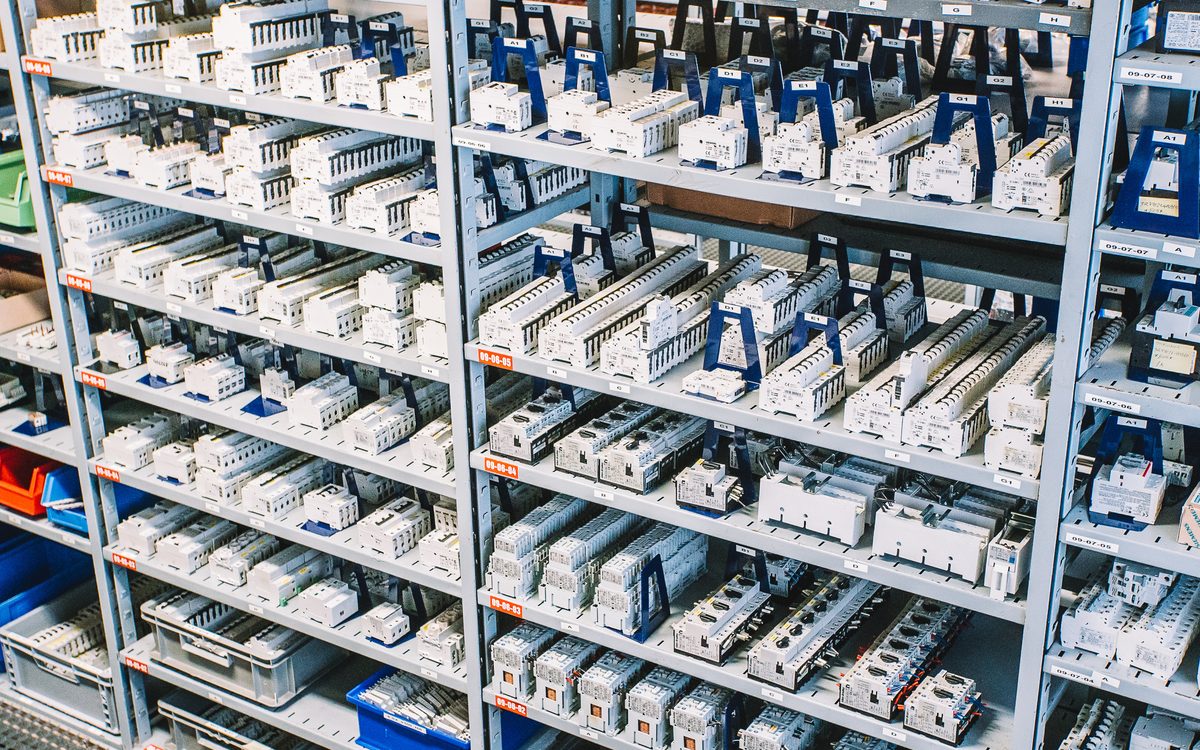 Rows of white circuit breakers and switchgear parts stacked on grey metal shelving