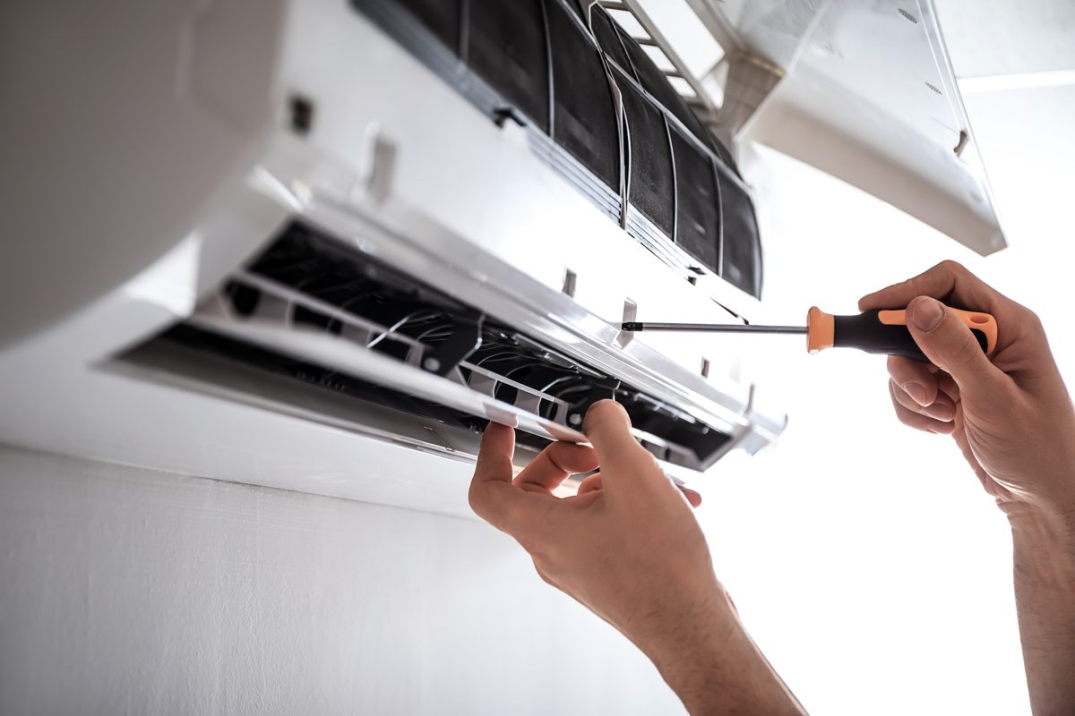 Hands using a screwdriver on the opened front of a white wall-mounted heat pump unit