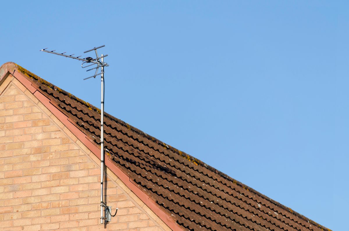 A TV aerial on a pole at the gable end of a brick house with a tiled roof, against a clear blue sky